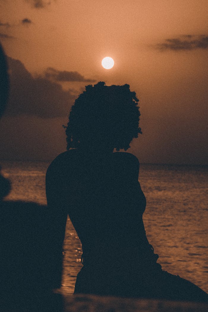 Offerings Silhouette of a woman sitting by the sea at sunset. Warm, relaxed atmosphere.